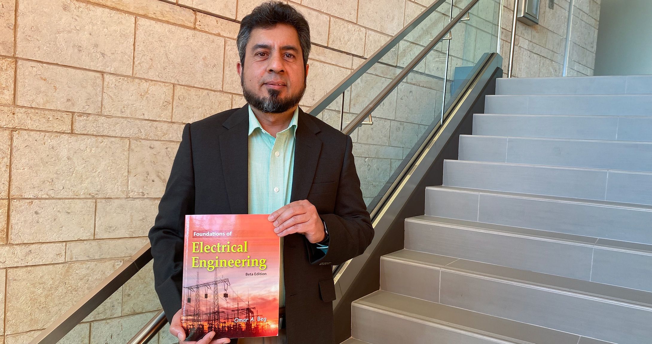 Dr. Omar Beg holding his book on stairwell at engineering building